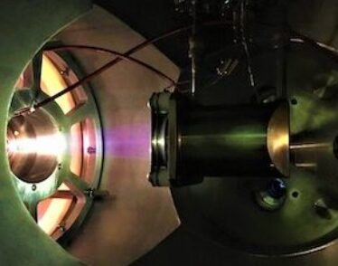 A picture of the ion source used by the IsoDAR cyclotron team, which shows the ion beam glowing inside their device.
