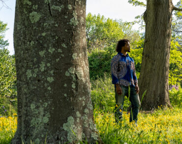 Photo of Makinde Ogunnaike standing, looking off to the right, between two large tree trunks