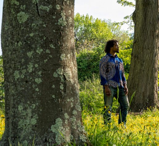 Photo of Makinde Ogunnaike standing, looking off to the right, between two large tree trunks