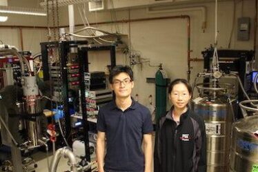 Physics postdoc and grad student stand in MIT lab.