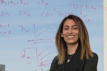 woman stands in front of window which has equations written on it.