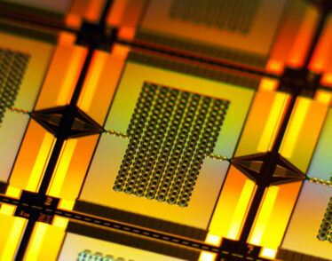 A yellow-lit closeup zooms in on one tiny, rectangular amplifier on the wafer. It has a chain-like rectangular grid in center that connects to the left and right edges of the wafer.
