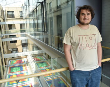 Senior Thomas Bergamaschi leans on a railing overlooking an indoor courtyard with a colorful floor