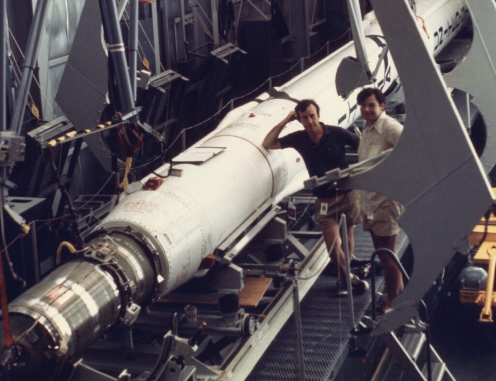 two men pose beside satellite prior to its launch