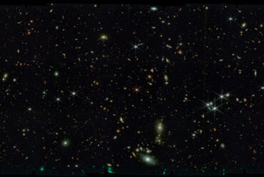 Black space with thousands of stars and tiny swirling galaxies.