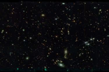 Black space with thousands of stars and tiny swirling galaxies.