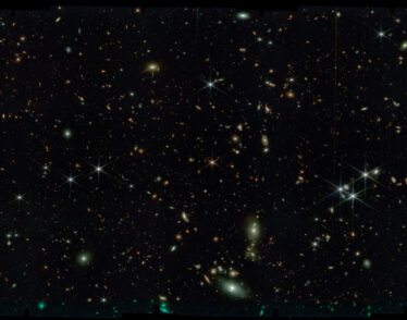 Black space with thousands of stars and tiny swirling galaxies.