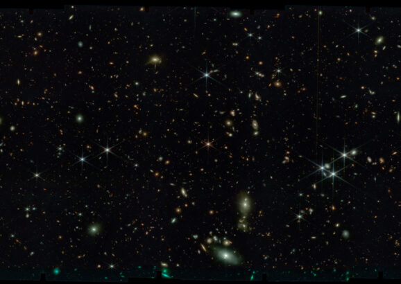Black space with thousands of stars and tiny swirling galaxies.