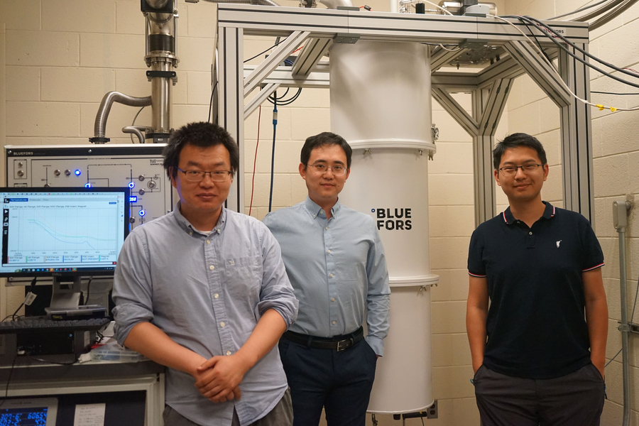 Three physicists pose inside lab beside computers and equipment
