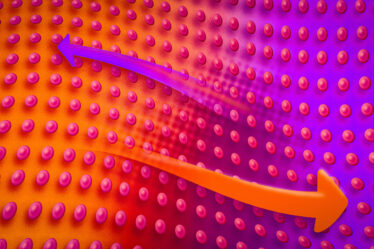 A wavey array of pink spheres floats like on water. A wavey orange arrow points to the right, and a wavey purple arrow points to the left.