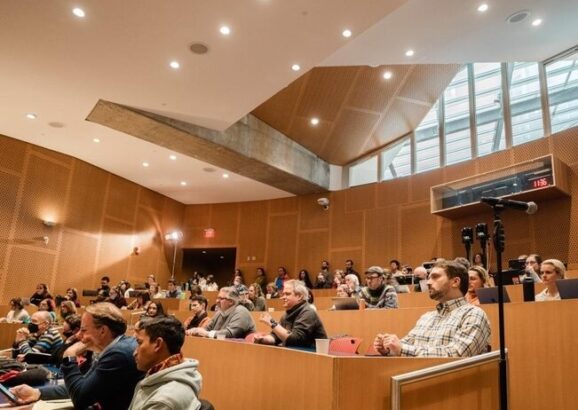 View of audience members in a lecture hall, who look to be listening intently to the panel discussions.