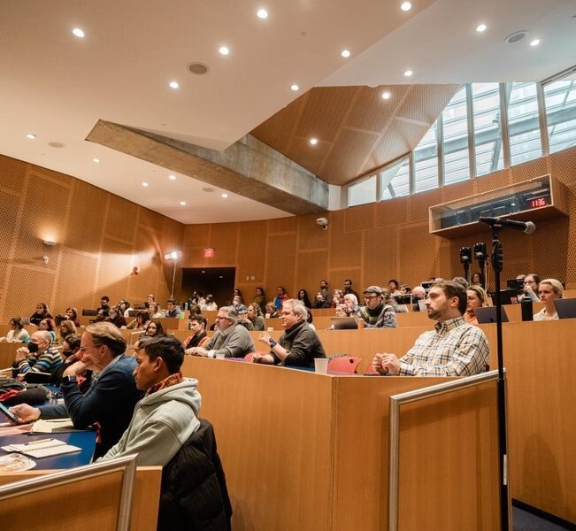 View of audience members in a lecture hall, who look to be listening intently to the panel discussions.