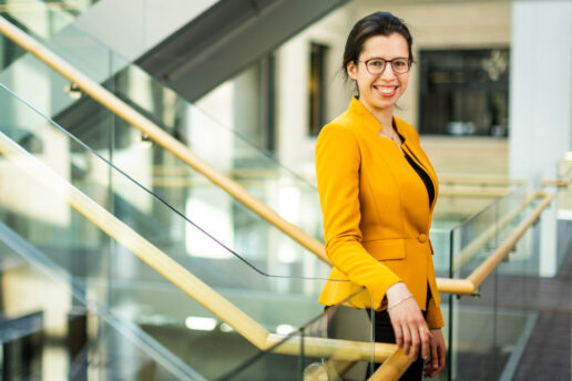 Netta Engelhardt stands near stairway for a portrait. Dramatic diagonal shapes are created by the stairways and glass railings.