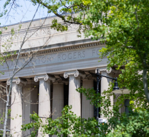 The columns of Building 7 are visible through green foliage on a sunny Spring day.