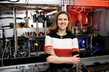 Olivia Rosenstein stands with arms folded in front of a large piece of lab equipment