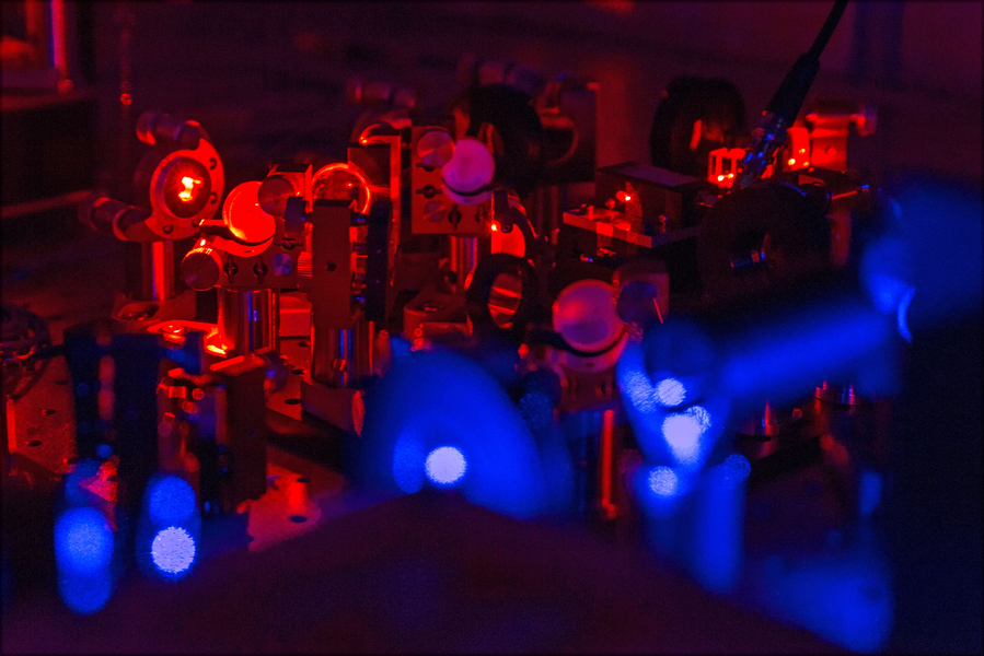 Blue and red-tinted photo shows lots of lasers and lenses on a table.
