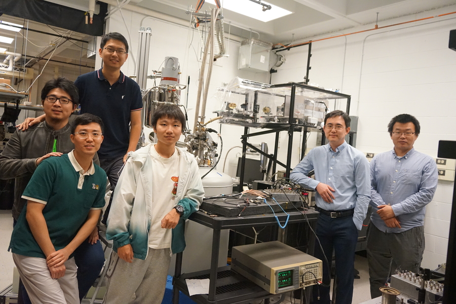 Six men pose amidst equipment in a small lab