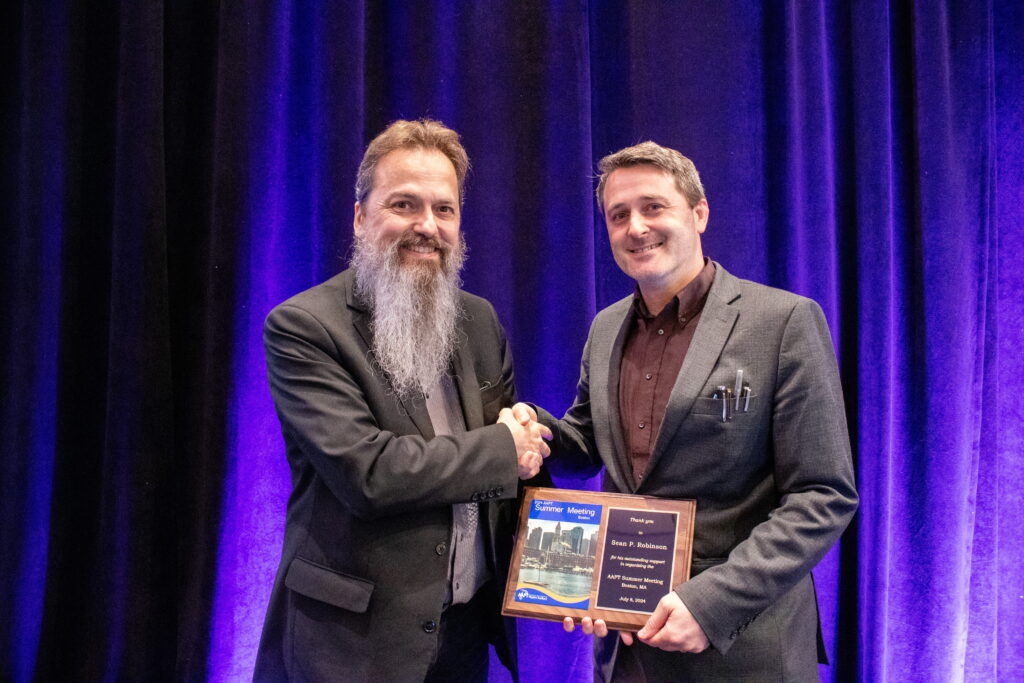 two men, one receiving an award plaque, pose together