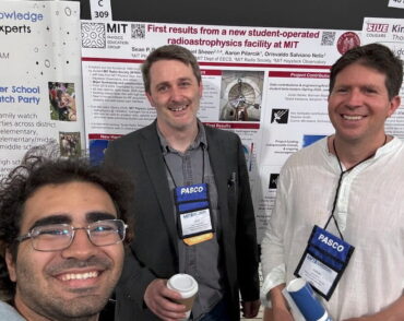 three people pose in front of physics posters