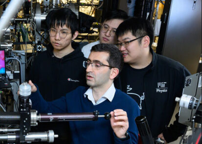 Professor Nuh Gedik, surrounded by students, stand looking at an experiment