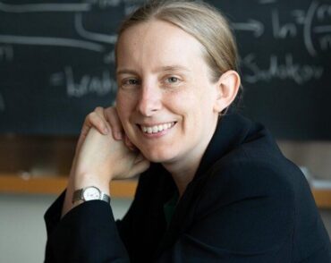 Tracy Slatyer poses in front of blackboard covered in physics equations