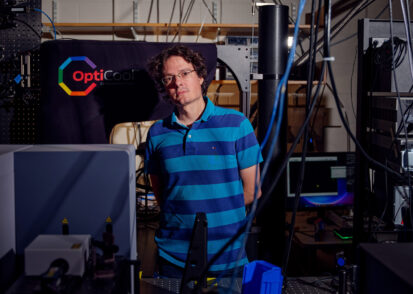 Riccardo Comin stands in his lab, filled with cables and large equipment.