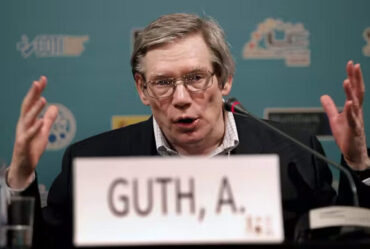 Alan Guth sits speaking animatedly on a panel