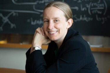 Tracy Slatyer poses in front of blackboard covered in physics equations