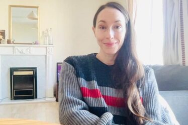 Bia Adams sitting in a tidy living room and smiling, wearing a bulky sweater