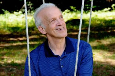 Daniel Kleppner, a white-haired man wearing a blue short-sleeved shirt, sits on what appears to be some kind of swing.