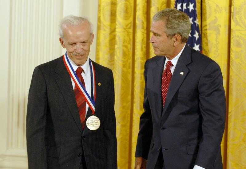 Daniel Kleppner, with a medal around his neck, stands next to George W. Bush before a yellow curtain.
