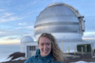 woman poses in front of a large telescope at observatory