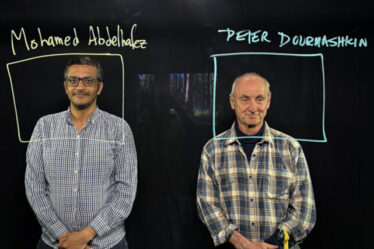 Photo of professors Mohamed Abdelhafez and Peter Dourmashkin drawing frames around themselves with their names using a transparent dry erase board