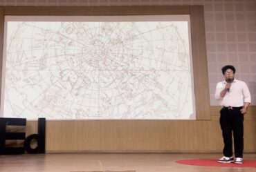 Vivan Mirchandani speaks in front of a screen, which shows graphics of constellations. A 