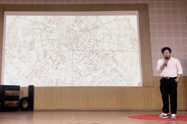 Vivan Mirchandani speaks in front of a screen, which shows graphics of constellations. A 
