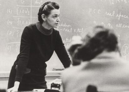 black and white image of Milliie Dresselhaus leaning forward on a desk in front of a chalkboard