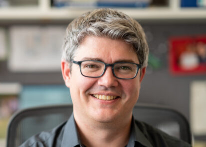 Professor Michael McDonald smiles while sitting at his desk, with blurry office background.