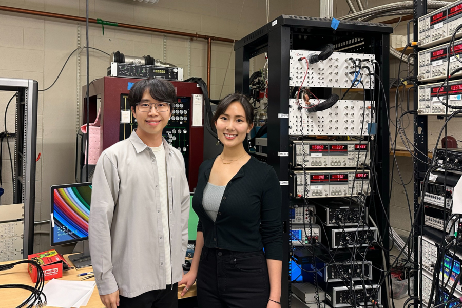 two people pose in front of large scientific equipment in a lab