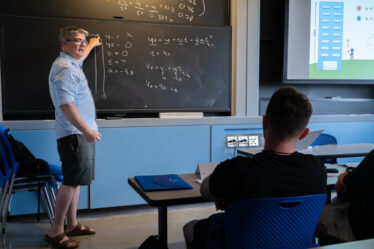 Professor stands at a chalkboard, lecturing in a classroom