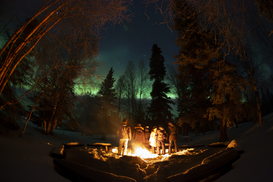 Group of people standing around fire pit at night, taken with an all-sky camera that greatly distorts the borders