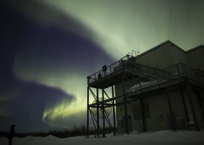 Aurora visible above a building and observation platform with two people silhouetted at night