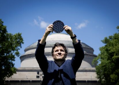 Man stands in front of the MIT dome, holding a circular wafer displaying moire patterns over his head
