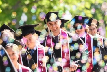 graduating MIT students in caps and gowns with one student looking straight at camera