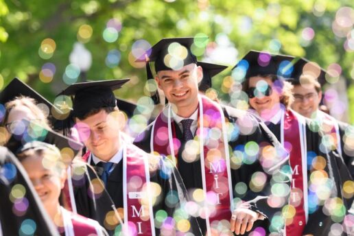 graduating MIT students in caps and gowns with one student looking straight at camera