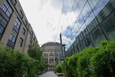Walkway with a brick building at left and a glass-walled building at right, with the MIT Dome between and beyond them
