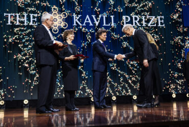 Kavli Prize laureate shaking hands with an official on stage during the ceremony while two other laureates look on.
