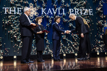 Kavli Prize laureate shaking hands with an official on stage during the ceremony while two other laureates look on.