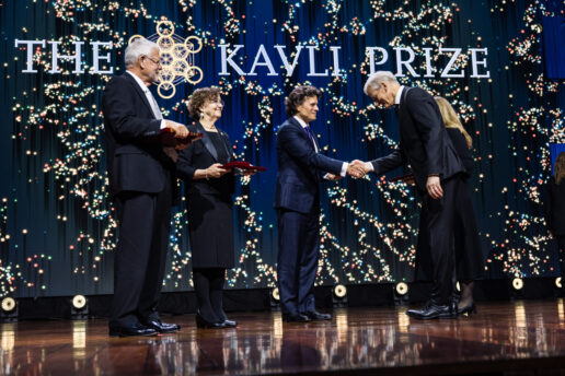 Kavli Prize laureate shaking hands with an official on stage during the ceremony while two other laureates look on.