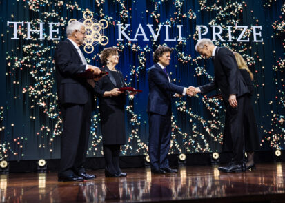 Kavli Prize laureate shaking hands with an official on stage during the ceremony while two other laureates look on.