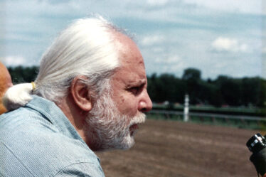 Profile photograph of A. Neil Pappalardo '64 with white hair in a ponytail, a white beard, and wearing a striped light blue button-down shirt.